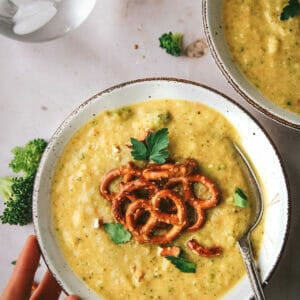 bowl of vegan broccoli cheddar soup topped with pretzels