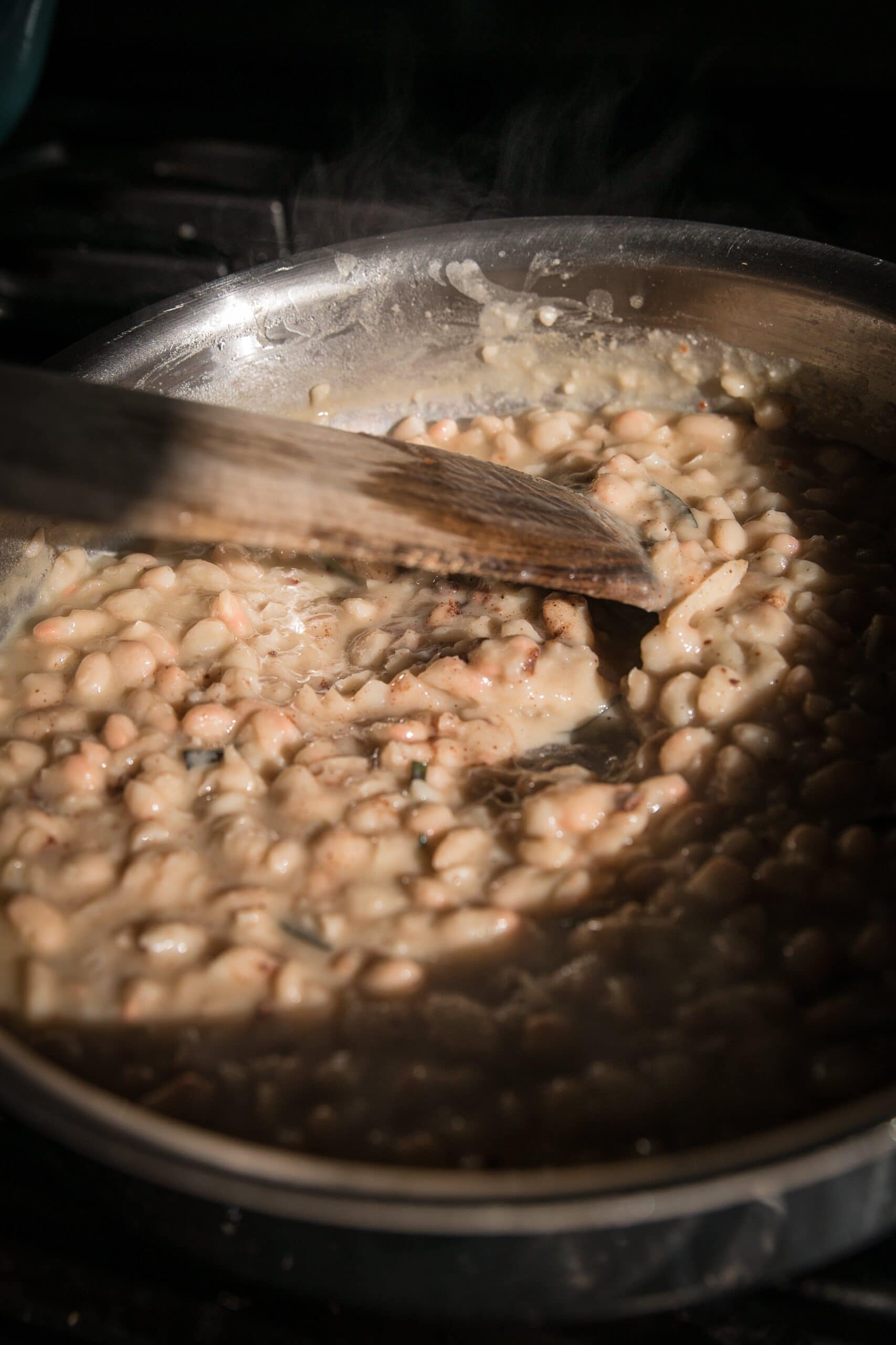 stirring a pot of braised white beans with a wooden spoon